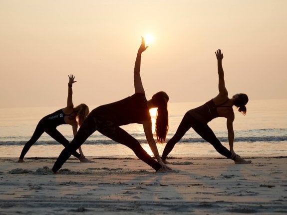 three women silhouetted against the sun, doing yoga on the beach