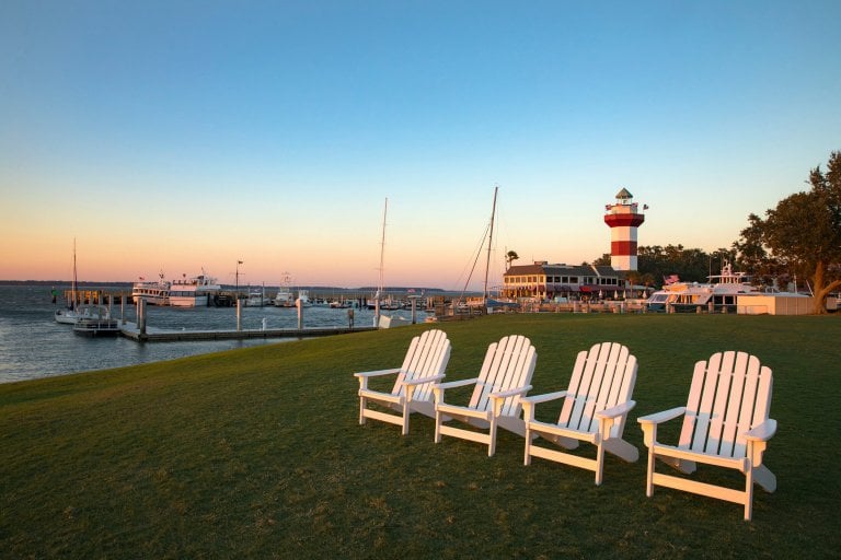 white wooden chairs in a line on golf course, harbourtown lighthouse in the background