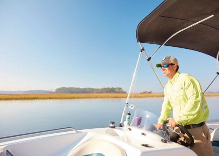 Man in green windbreaker smiles at helm of motorboat