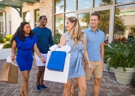 two couples smile as they walk down the street with shopping bags
