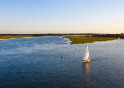 Sailboat with white sails glides along lowlands in Hilton Head Island