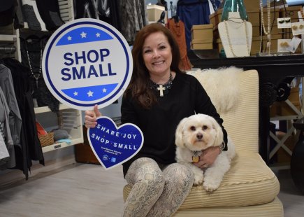 Woman smiles with small white dog and holds sign that reads shop small