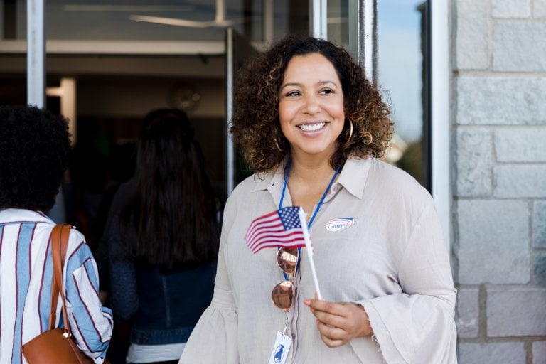 Woman smiles, holding American flag as she waits to vote