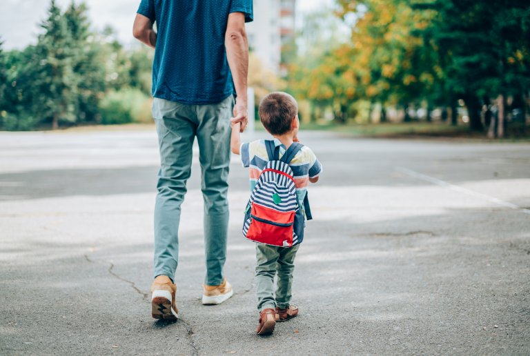 father and son walk toward school, the boy has a red backpack