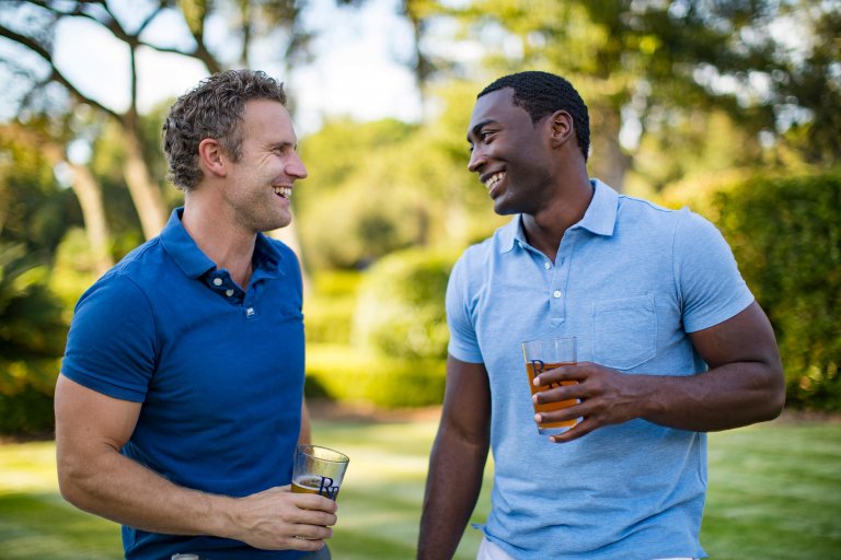 Two men smile and laugh as they drink beer on the green of a golf course