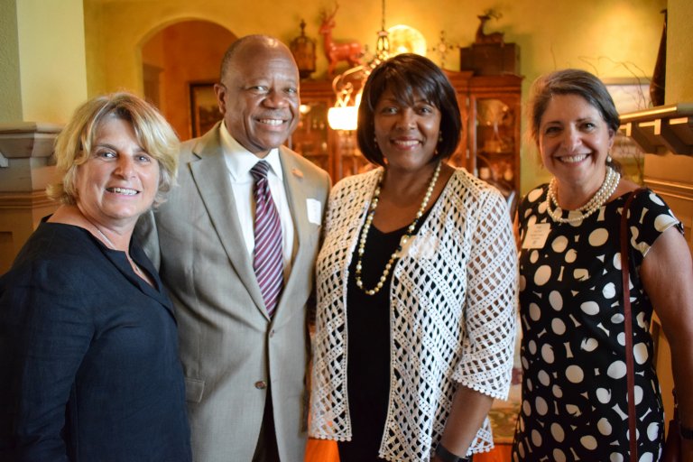 three women and one man pose and smile for a photo in business attire