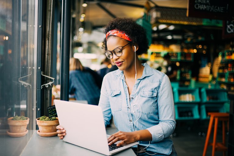 woman wearing red bandana works on her laptop in a coffee shop