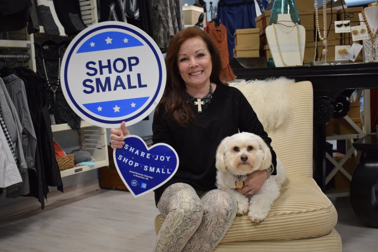 Woman smiles with small white dog and holds sign that reads shop small