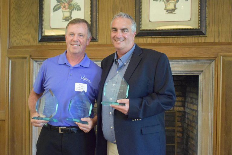 two middle aged men hold glass awards and smile